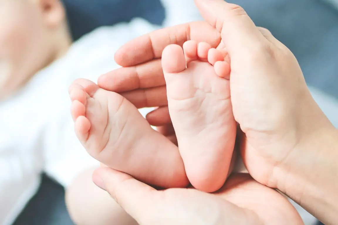 Zwei Frauenh&auml;nde die die F&uuml;&szlig;e eines S&auml;uglings halten